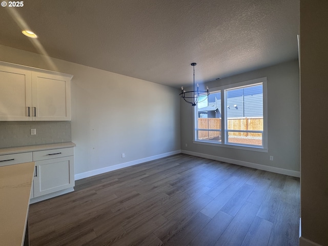 unfurnished dining area with a chandelier, baseboards, dark wood-type flooring, a textured ceiling, and recessed lighting