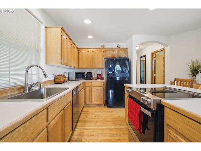 kitchen with a sink, light countertops, arched walkways, light wood-style flooring, and stainless steel appliances