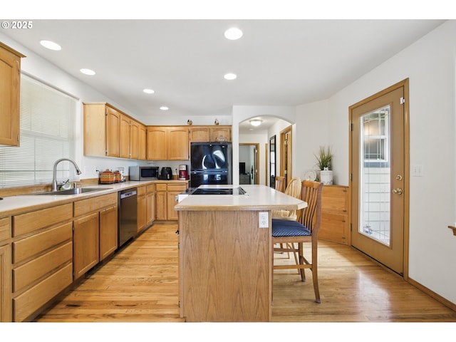 kitchen with a sink, a breakfast bar area, arched walkways, light wood-style flooring, and stainless steel appliances