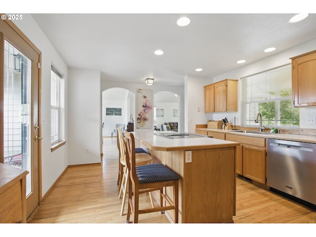 kitchen with a center island, stainless steel dishwasher, a sink, light countertops, and light wood-style floors