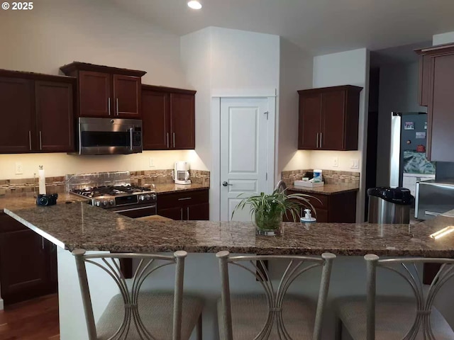 3625 Snowberry Rd, Eugene, OR 97403 - kitchen with appliances with stainless steel finishes, dark stone counters, a kitchen bar, dark brown cabinetry, and recessed lighting