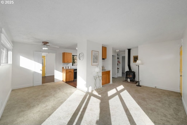 unfurnished living room with ceiling fan, a wood stove, light carpet, and a textured ceiling