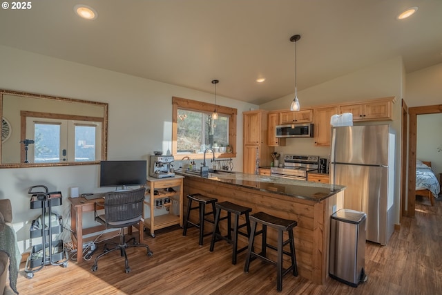 kitchen featuring wood-type flooring, lofted ceiling, dark stone counters, hanging light fixtures, and stainless steel appliances