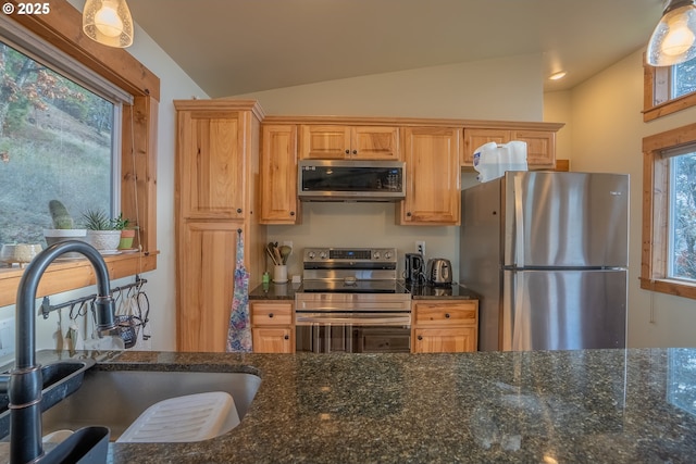 kitchen with lofted ceiling, sink, pendant lighting, appliances with stainless steel finishes, and dark stone countertops