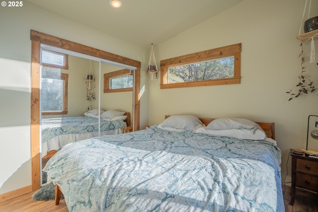 bedroom featuring a closet, wood-type flooring, vaulted ceiling, and multiple windows