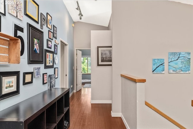 hallway featuring an upstairs landing, baseboards, track lighting, dark wood-style floors, and high vaulted ceiling