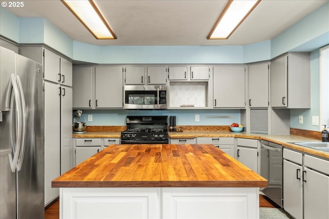 kitchen featuring appliances with stainless steel finishes, butcher block countertops, a kitchen island, and gray cabinetry