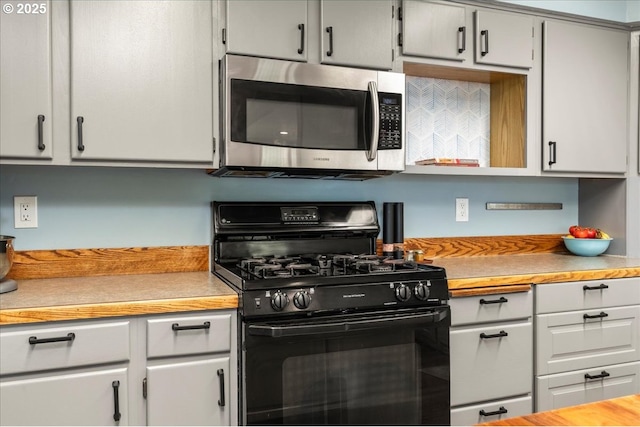 kitchen with black range with gas stovetop, stainless steel microwave, light countertops, tasteful backsplash, and white cabinetry