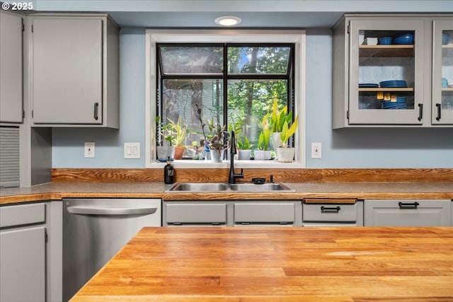 kitchen featuring dishwasher, a sink, wood counters, and glass insert cabinets