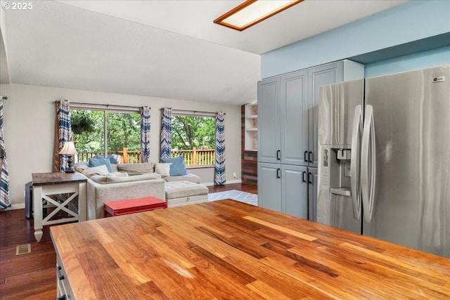 kitchen featuring stainless steel refrigerator with ice dispenser, wooden counters, dark wood-type flooring, baseboards, and open floor plan