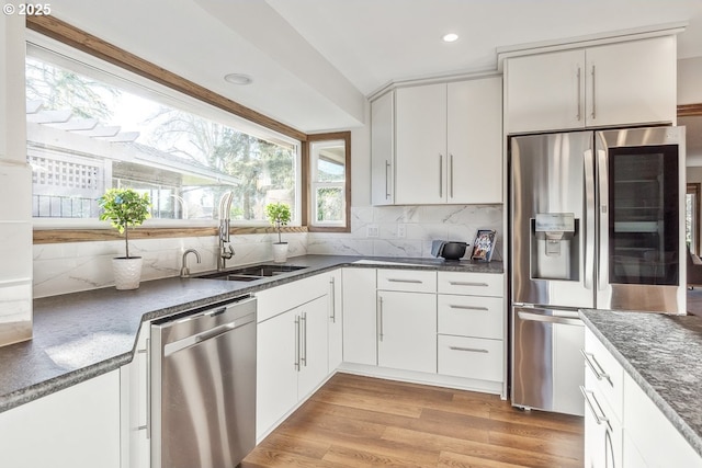 kitchen featuring decorative backsplash, appliances with stainless steel finishes, sink, white cabinets, and light hardwood / wood-style floors