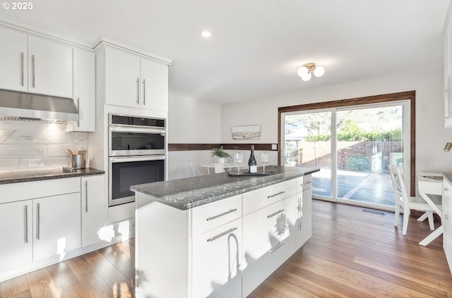 kitchen with white cabinets, decorative backsplash, light wood-type flooring, and double oven