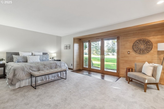 carpeted bedroom with access to exterior, wooden walls, and french doors