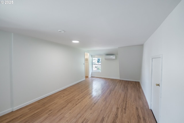 spare room featuring an AC wall unit, light wood finished floors, and baseboards