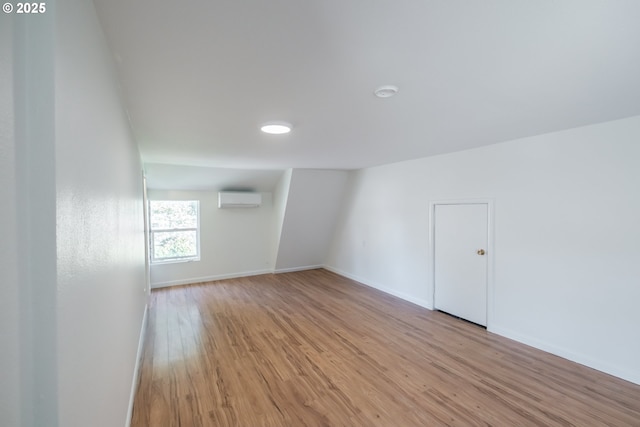 empty room featuring an AC wall unit, light wood-type flooring, and baseboards