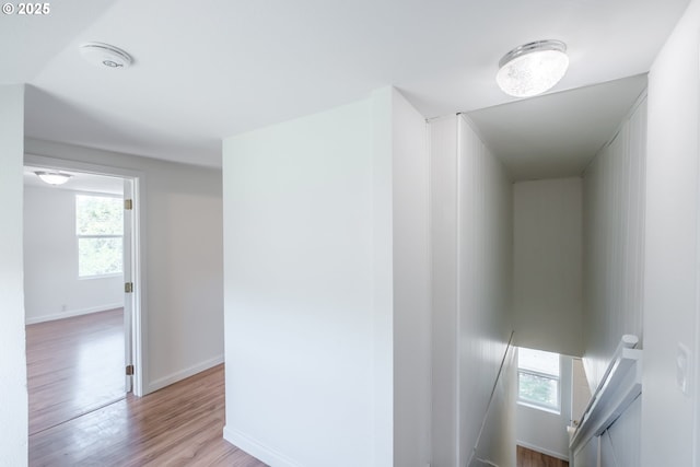 corridor with an upstairs landing, plenty of natural light, light wood-type flooring, and baseboards