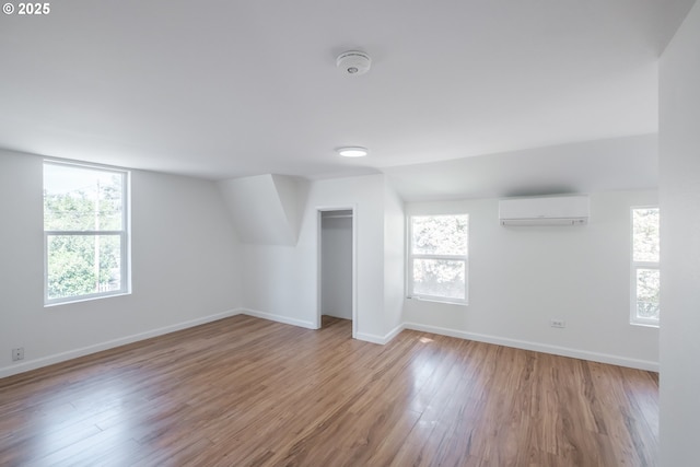 bonus room featuring an AC wall unit, baseboards, and wood finished floors