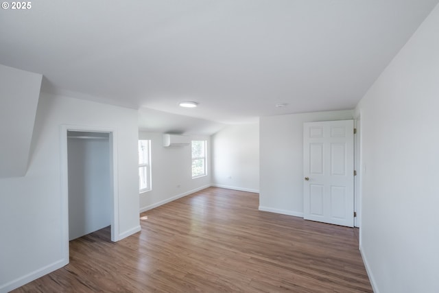 additional living space with an AC wall unit, light wood-style floors, and baseboards