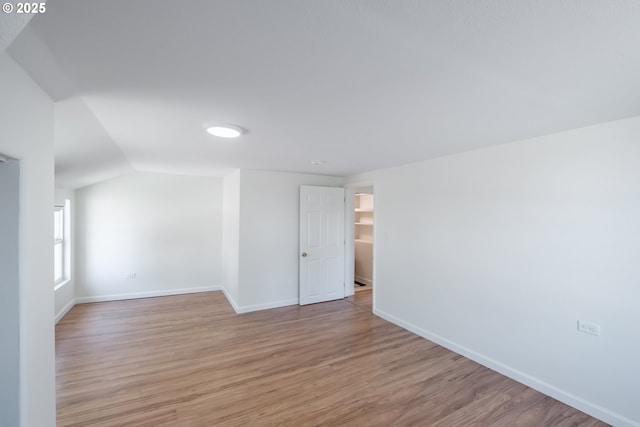 empty room featuring light wood-type flooring, baseboards, and vaulted ceiling