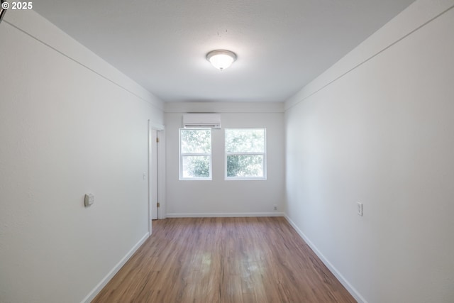 empty room with a wall mounted air conditioner, wood finished floors, and baseboards