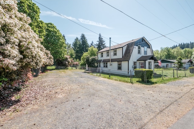 view of front of house featuring fence, a gambrel roof, driveway, and roof with shingles