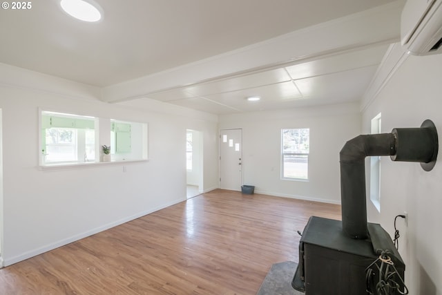 living area featuring an AC wall unit, light wood finished floors, baseboards, a wood stove, and beamed ceiling