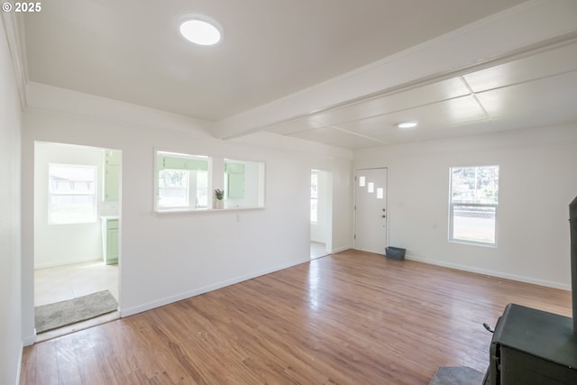 unfurnished living room featuring healthy amount of natural light, light wood-style floors, baseboards, and beam ceiling