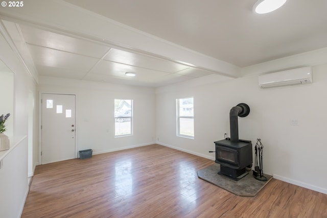 unfurnished living room featuring a wall mounted AC, light wood finished floors, baseboards, a wood stove, and beam ceiling