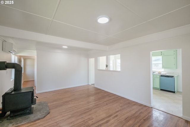unfurnished living room with light wood-style flooring, an AC wall unit, baseboards, and a wood stove
