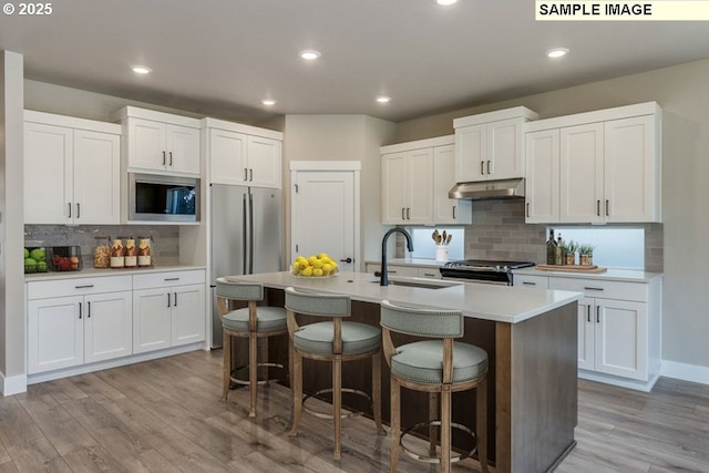 kitchen with under cabinet range hood, a kitchen breakfast bar, stainless steel appliances, and a sink