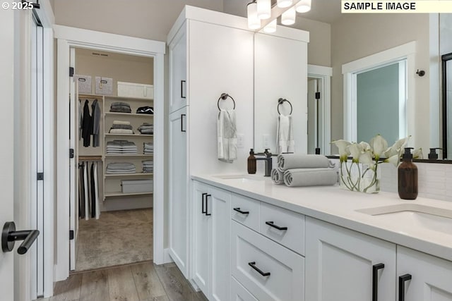 bathroom featuring wood finished floors, double vanity, a sink, a spacious closet, and a chandelier