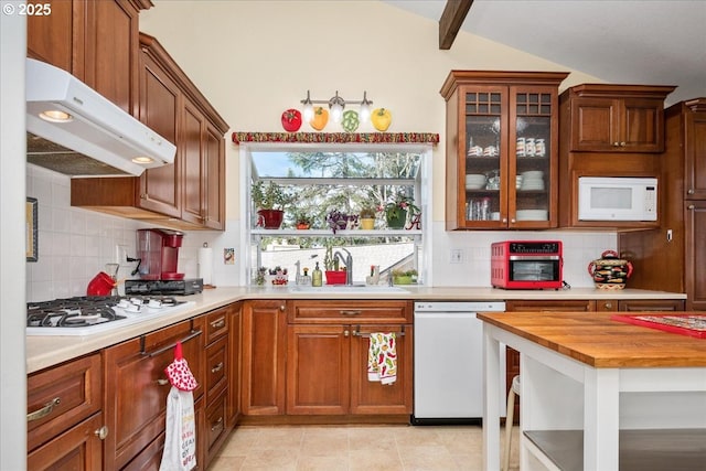 kitchen with tasteful backsplash, vaulted ceiling, a sink, white appliances, and under cabinet range hood