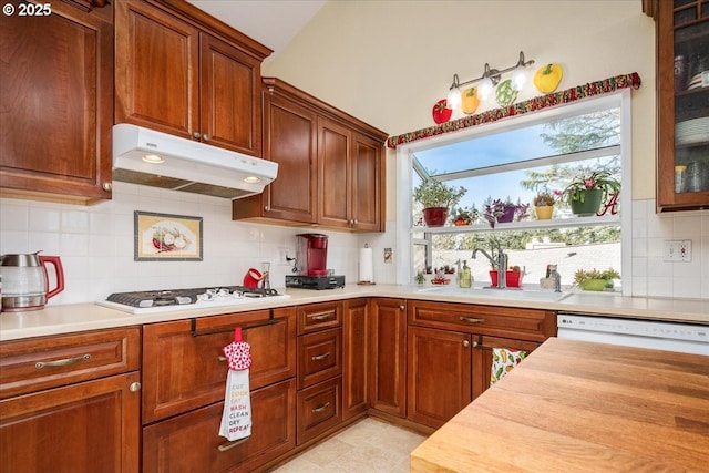 kitchen with white appliances, glass insert cabinets, a sink, under cabinet range hood, and backsplash