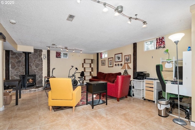 living room featuring a wood stove, visible vents, a textured ceiling, and light tile patterned floors