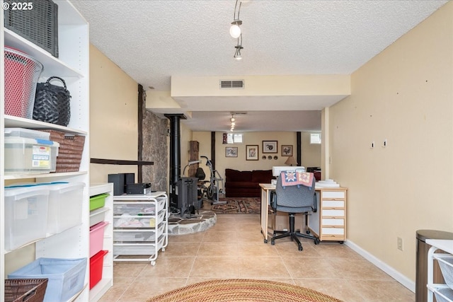 tiled office space featuring a wood stove, visible vents, a textured ceiling, and baseboards