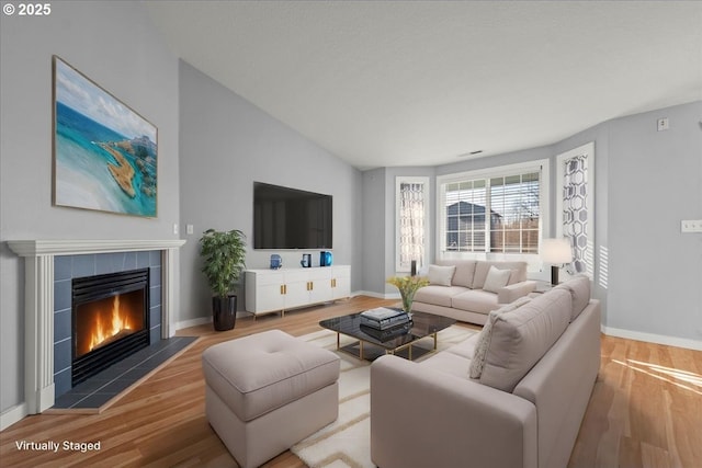 living room with lofted ceiling, a tiled fireplace, and hardwood / wood-style floors