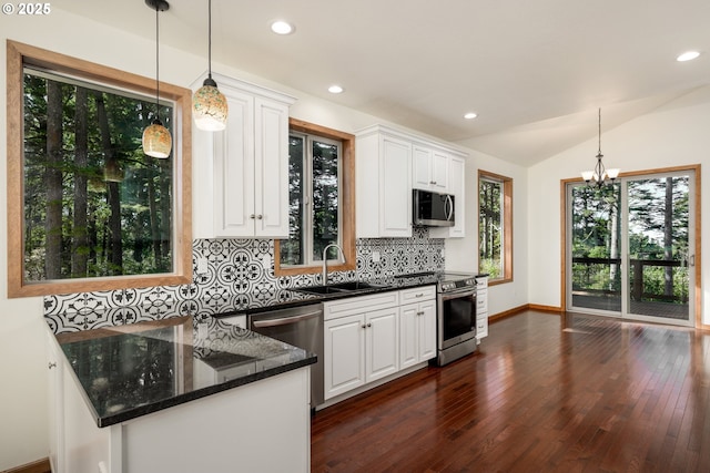 kitchen with stainless steel appliances, a sink, white cabinetry, vaulted ceiling, and backsplash