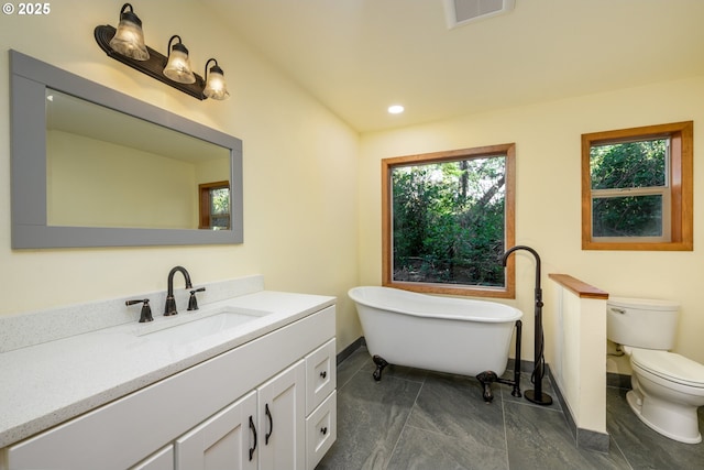 bathroom with toilet, vanity, visible vents, a freestanding bath, and baseboards