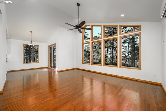 unfurnished living room with hardwood / wood-style flooring, an AC wall unit, high vaulted ceiling, baseboards, and ceiling fan with notable chandelier