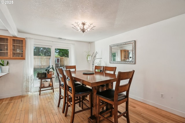 dining room with an inviting chandelier, baseboards, light wood finished floors, and a textured ceiling