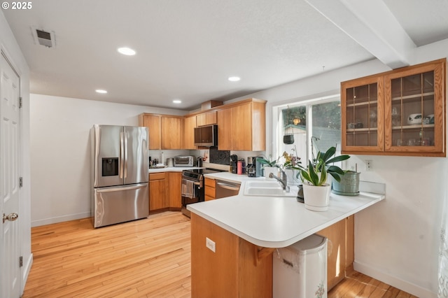 kitchen featuring a sink, baseboards, a peninsula, light wood-style floors, and stainless steel appliances