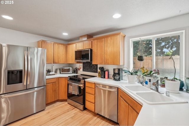 kitchen with tasteful backsplash, light wood-type flooring, a sink, light countertops, and stainless steel appliances