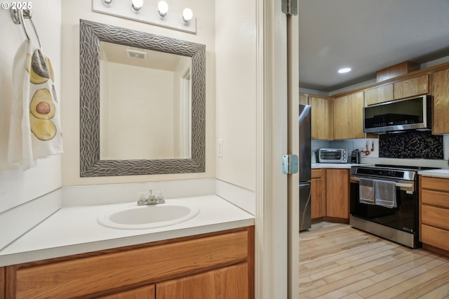 kitchen with brown cabinetry, light countertops, a sink, light wood-style flooring, and stainless steel appliances