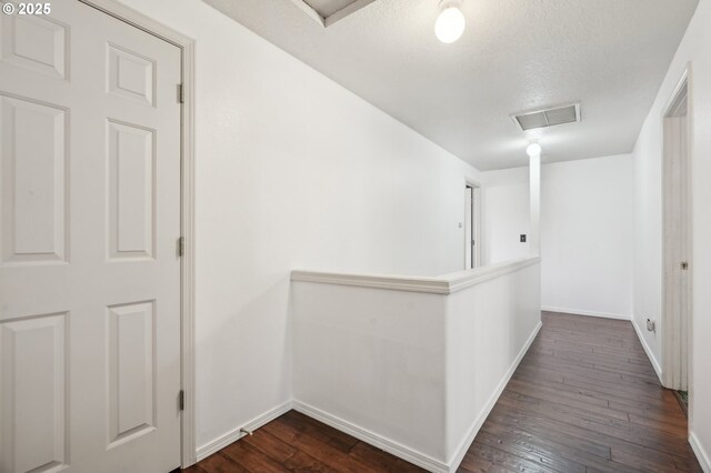 corridor featuring visible vents, baseboards, attic access, dark wood finished floors, and an upstairs landing