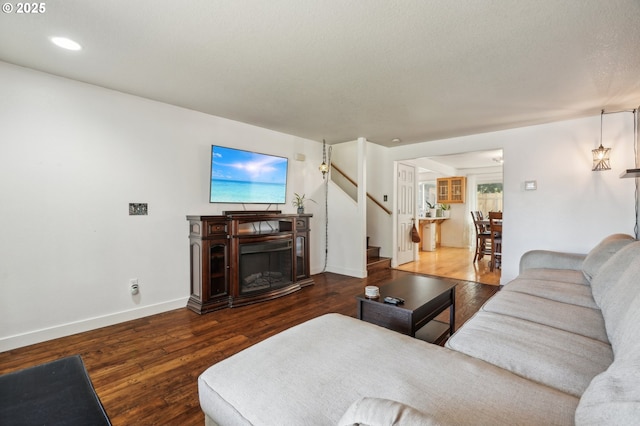 living room with a glass covered fireplace, recessed lighting, baseboards, wood finished floors, and stairway