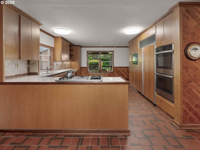 18036 NW Emmaus Ln, Portland, OR 97231 - kitchen featuring stainless steel double oven, stovetop, wooden walls, paneled built in refrigerator, and a peninsula
