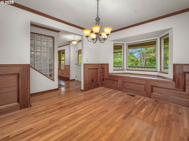 18036 NW Emmaus Ln, Portland, OR 97231 - unfurnished dining area featuring crown molding, a chandelier, light wood-type flooring, a wainscoted wall, and a textured ceiling