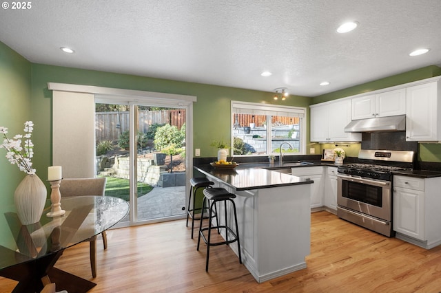 kitchen featuring a breakfast bar area, white cabinets, kitchen peninsula, stainless steel gas range, and light wood-type flooring