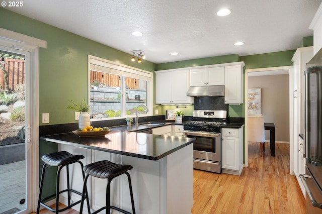 kitchen featuring sink, appliances with stainless steel finishes, white cabinetry, light hardwood / wood-style floors, and kitchen peninsula