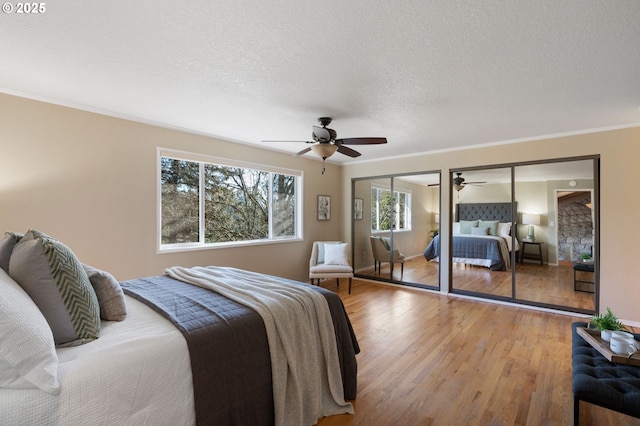 bedroom featuring a textured ceiling, ornamental molding, two closets, ceiling fan, and light hardwood / wood-style floors